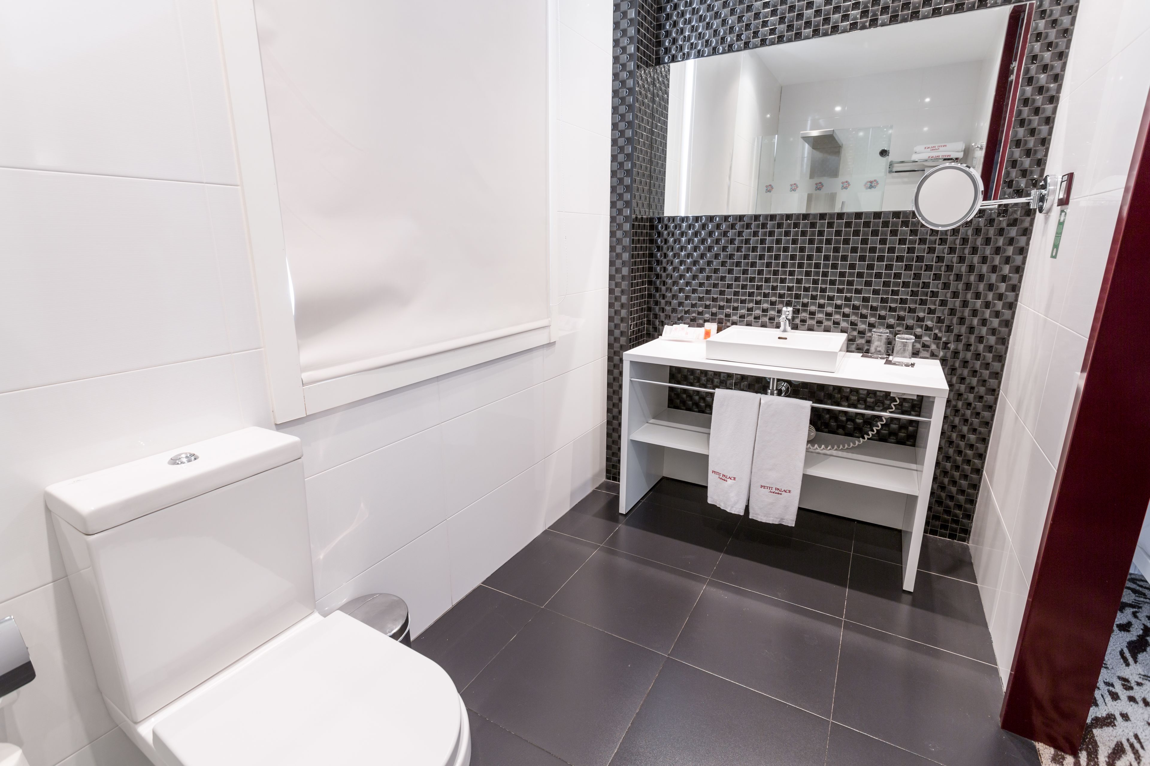 Un bany modern amb un vàter blanc, un lavabo amb mirall i una tovallola penjada a la paret.