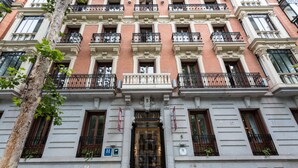 Un edificio de varios pisos con un estilo arquitectónico clásico, que presenta balcones con barandillas de hierro forjado, una entrada central con puerta de cristal y un hidrante a la vista en la planta baja.