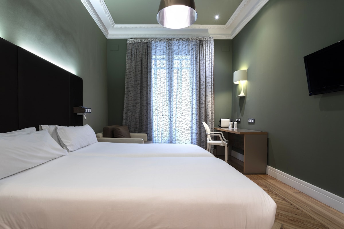 Habitación de hotel con una cama grande, un escritorio con silla, un televisor y una ventana con cortinas.
