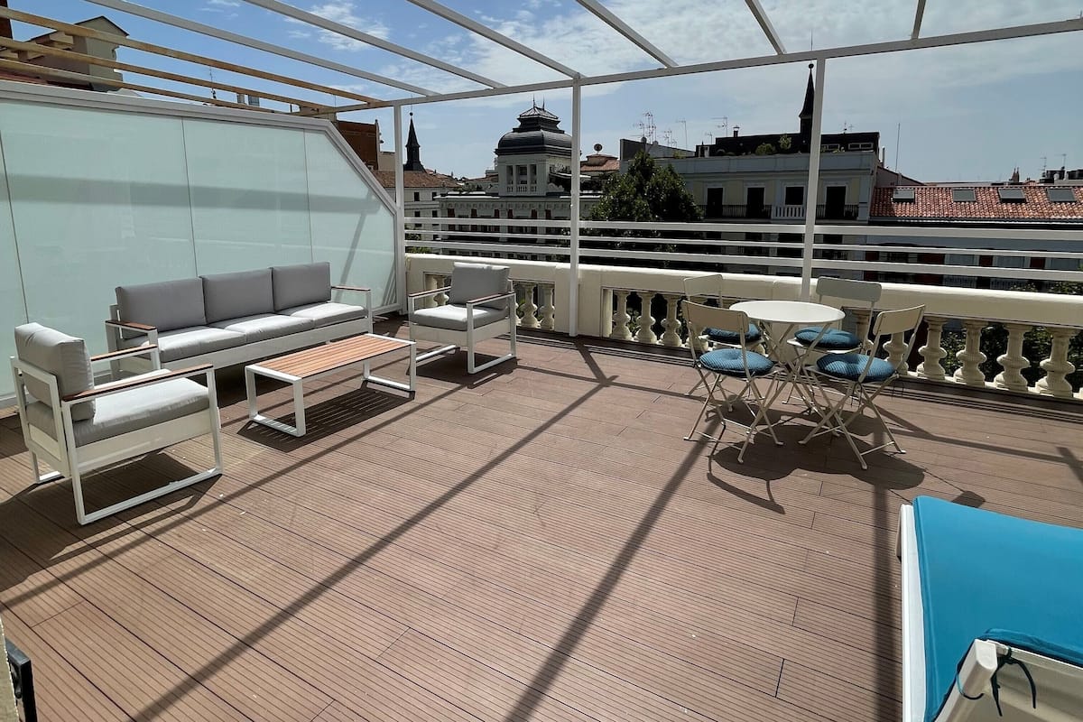 Terraza al aire libre iluminada por el sol con un sofá, sillas y una mesa.