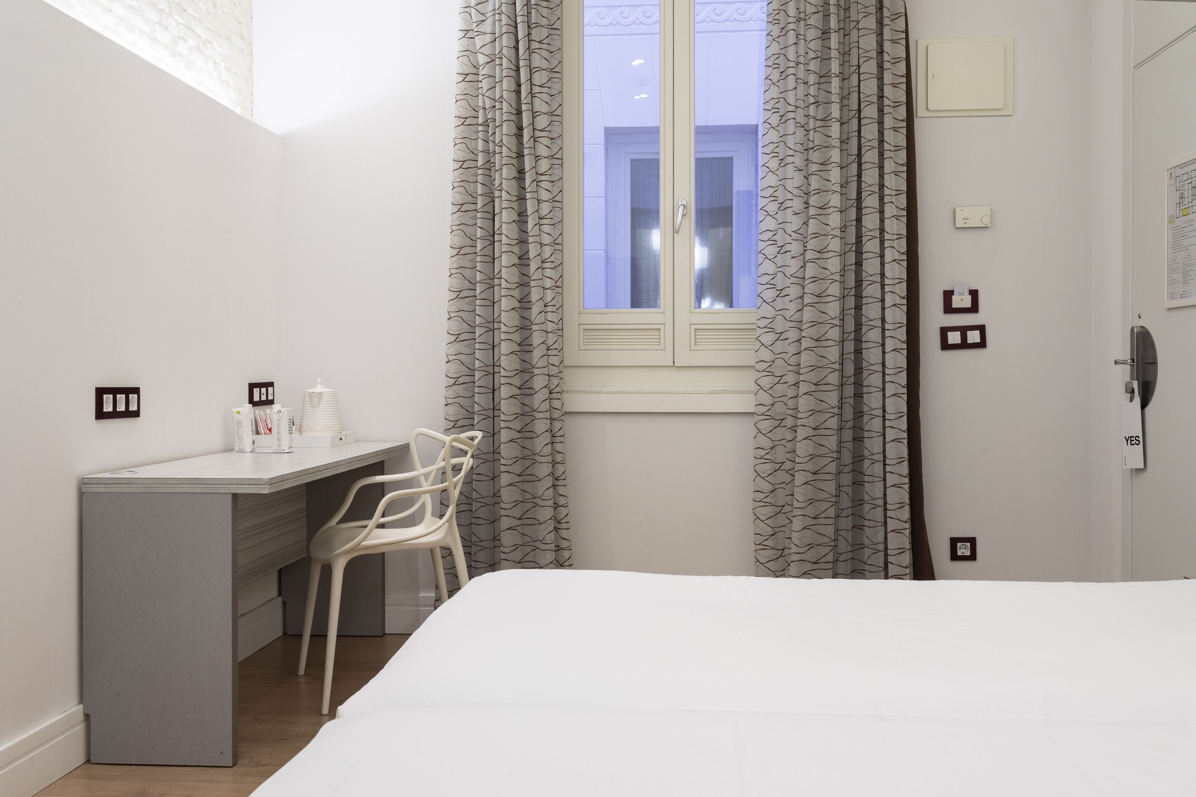 A bedroom with a bed, a desk, and a chair. There is a window with curtains.