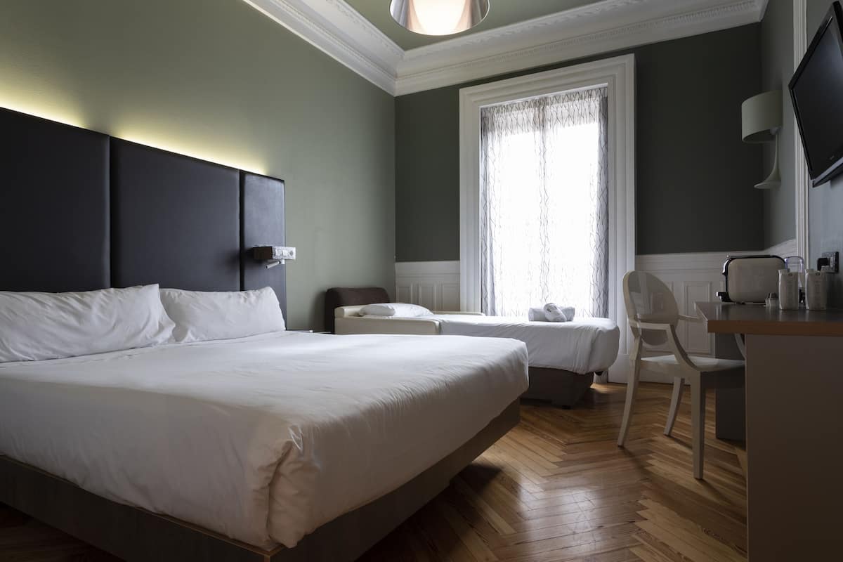 Habitación de hotel con una cama grande, dos camas más pequeñas, un escritorio, una silla y un televisor.