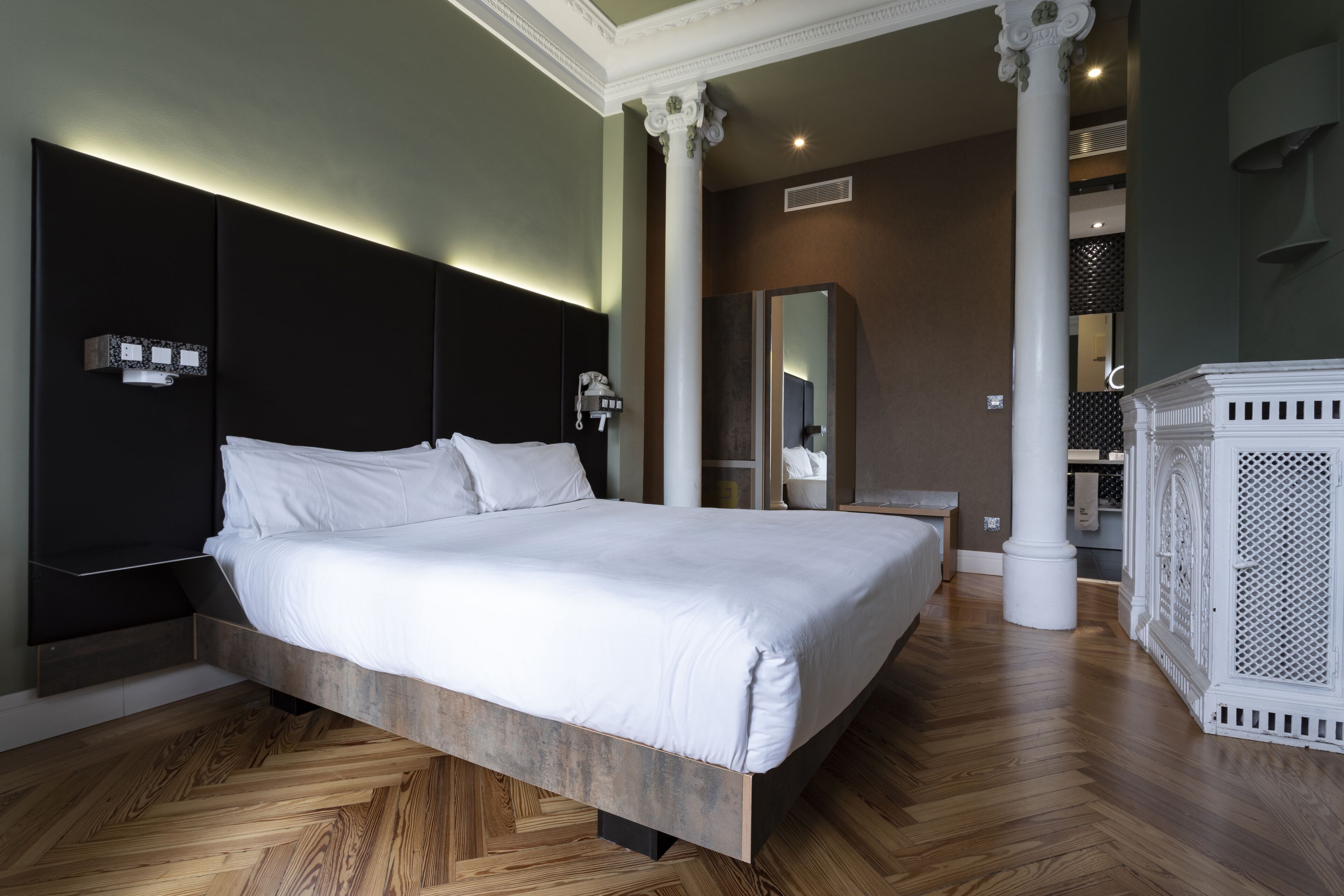 Un dormitorio moderno con una cama grande, suelo de madera y un espejo amplio.
