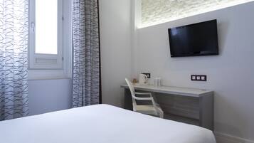 Habitación de hotel con cama, escritorio con silla, televisor de pantalla plana montado en la pared y ventana con cortinas estampadas.