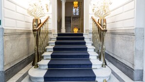 Una imponente escalera con escalones de mármol y barandillas de latón, que conduce a un espacio interior luminoso.
