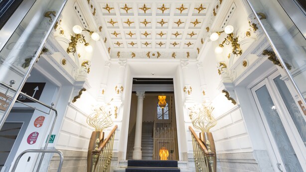 Imponente entrada con techo blanco y dorado, una escalera y barandillas ornamentales.