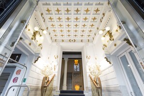 Imponente entrada con techo blanco y dorado, una escalera y barandillas ornamentales.
