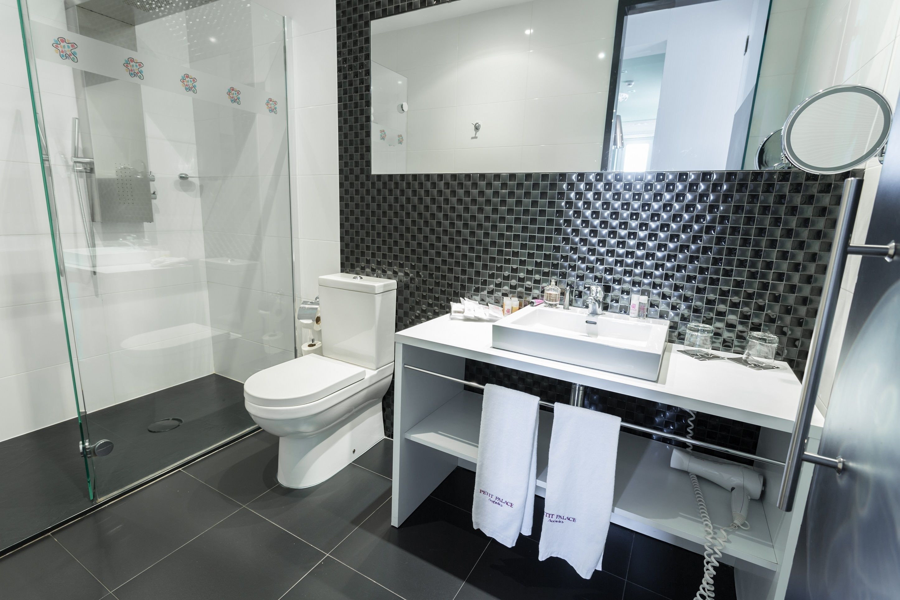 Ein modernes Badezimmer mit einer gläsernen Duschkabine, einer Toilette, einem Waschbecken mit Spiegel und einem Handtuchhalter mit Handtüchern.