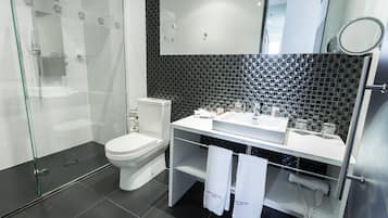 Ein modernes Badezimmer mit einer gläsernen Duschkabine, einer Toilette, einem Waschbecken mit Spiegel und einem Handtuchhalter mit Handtüchern.