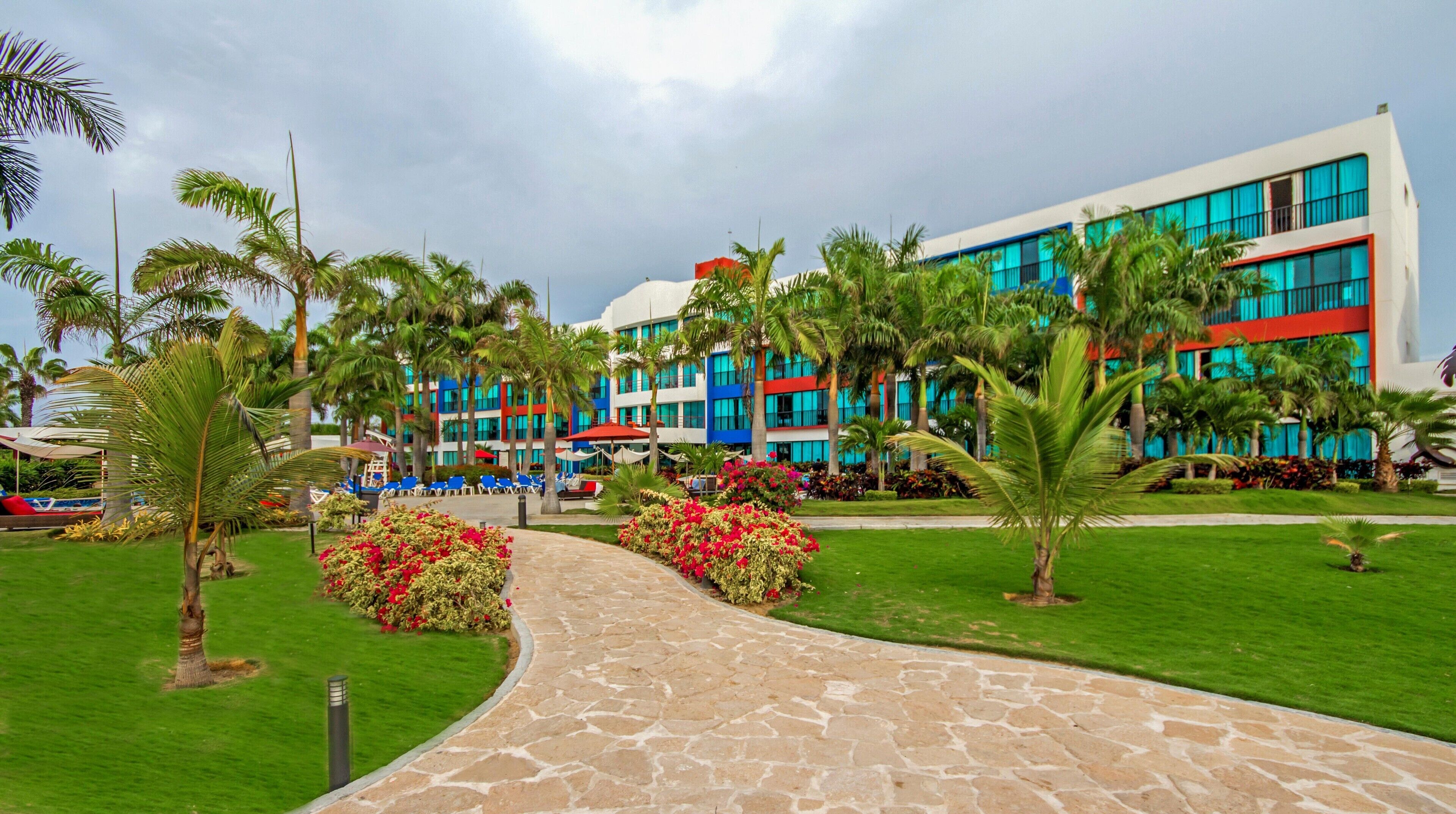 A hotel with a paved walkway, palm trees, and a multi-story building with large windows.