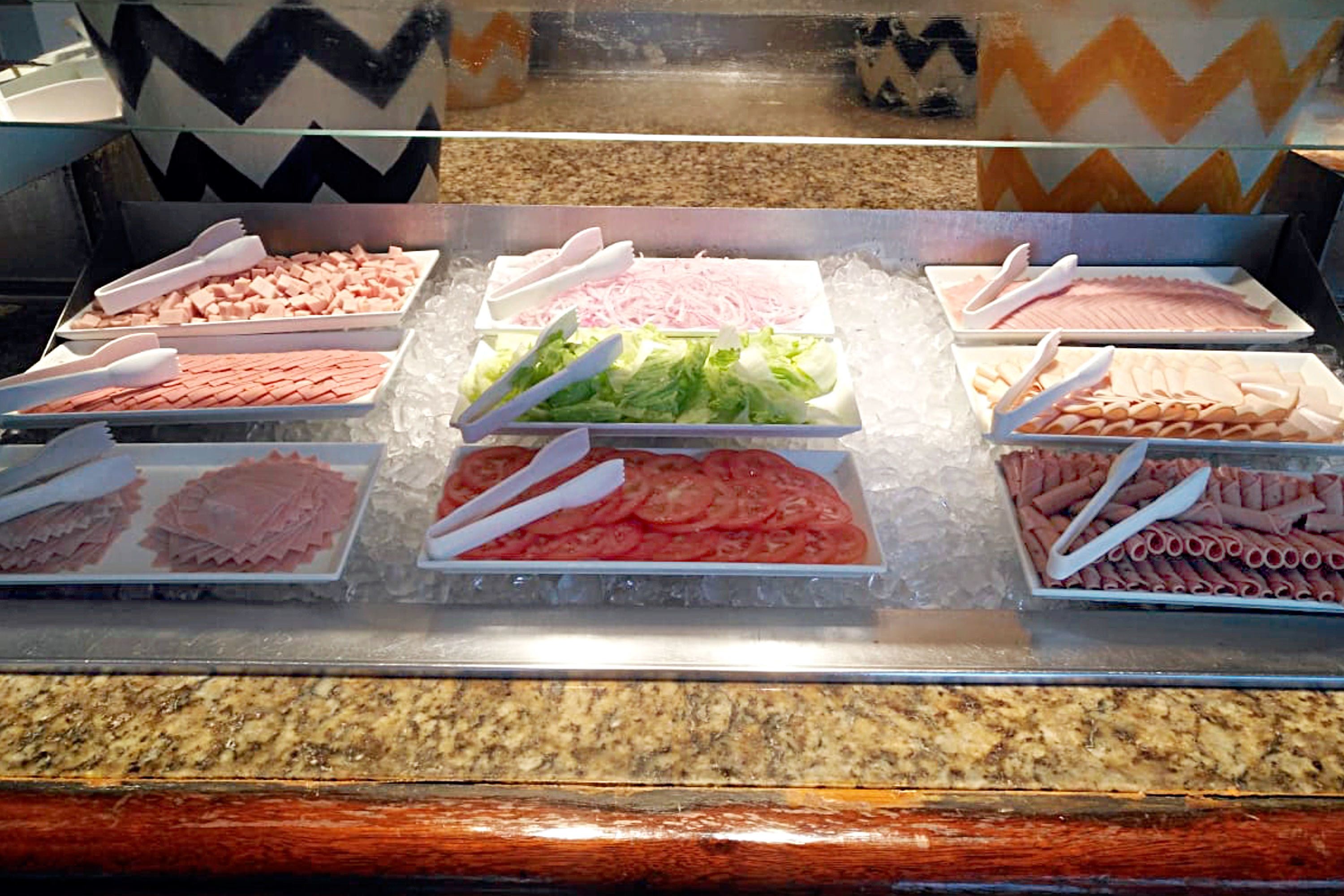 A buffet with various food items like sliced meats and vegetables, arranged on trays with serving utensils.
