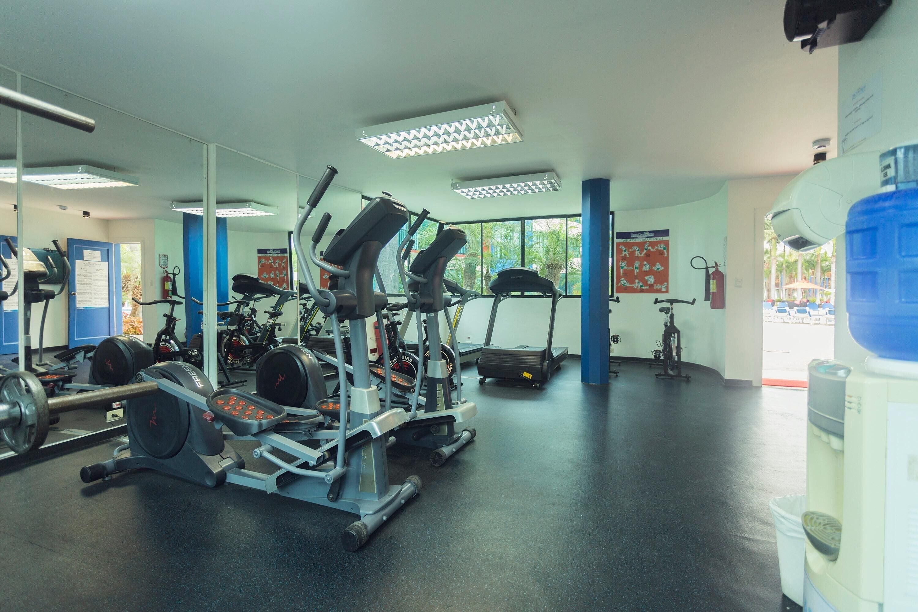 Une salle de sport équipée de matériel d’exercice, de miroirs et d’un distributeur d’eau.