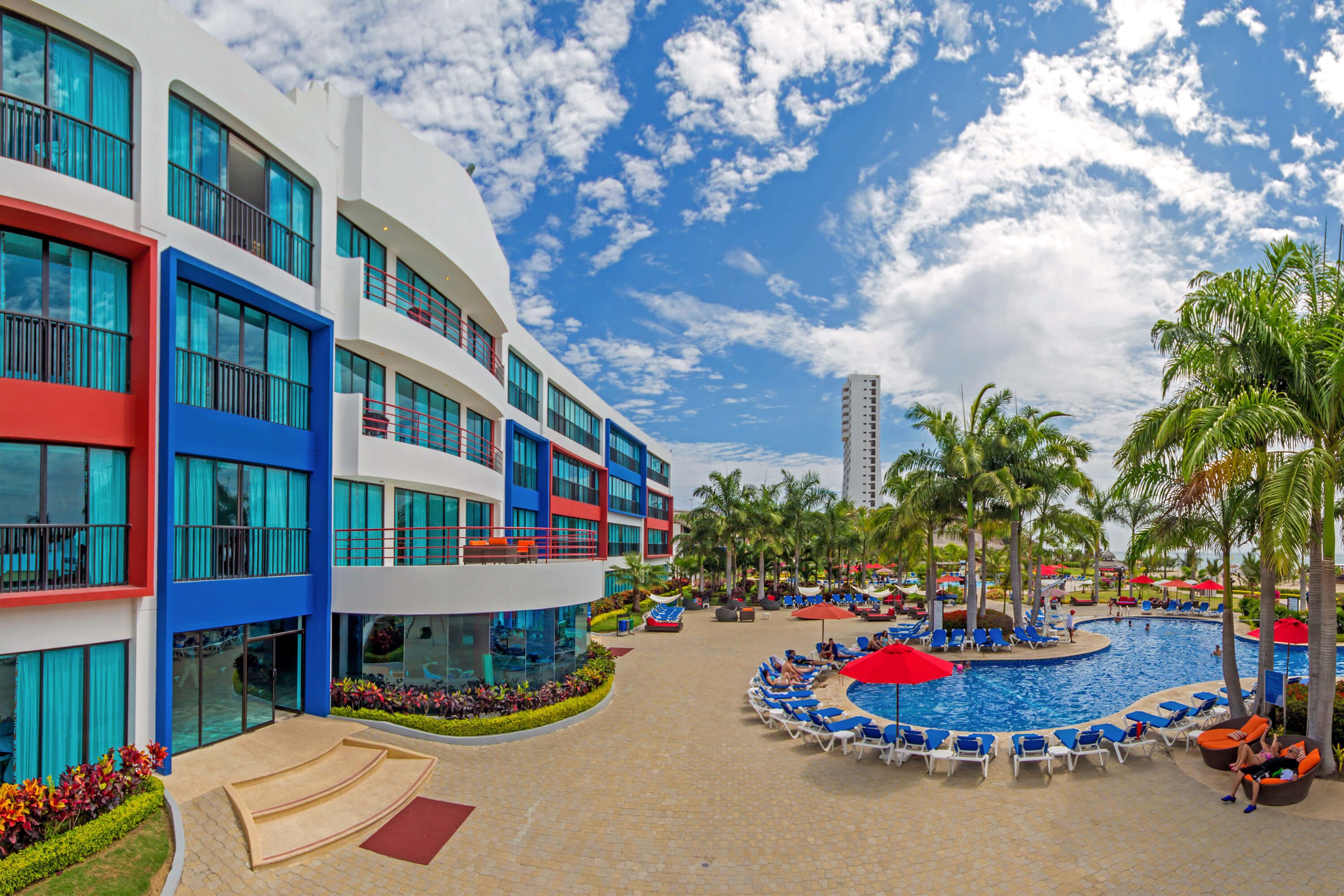 A resort with a swimming pool, palm trees, and a modern building with balconies.