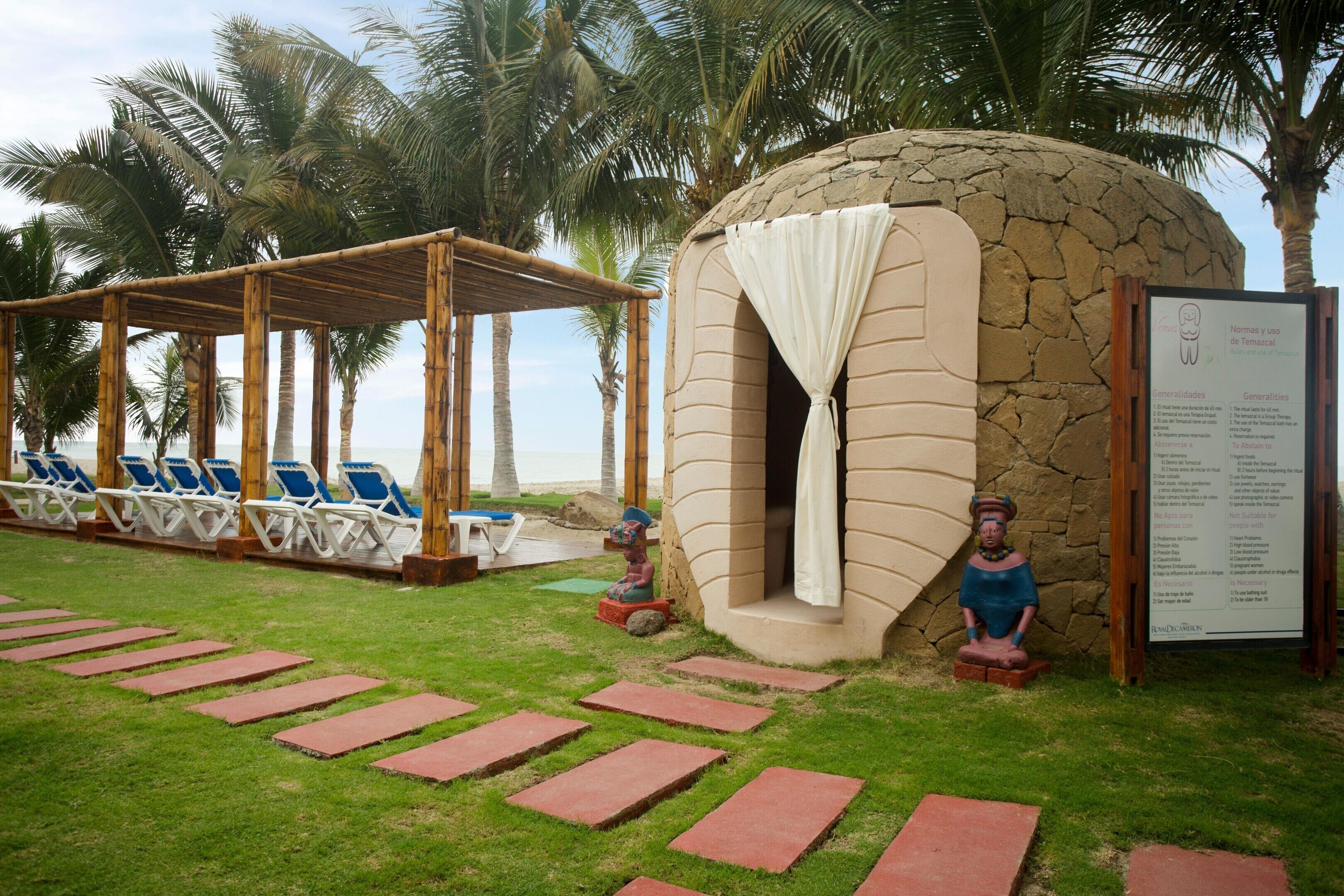 A beachside relaxation area with lounge chairs, a stone structure, and a sign with guidelines.