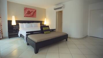A hotel room with a bed, bedside tables, an air conditioning unit, and a wall-mounted artwork.