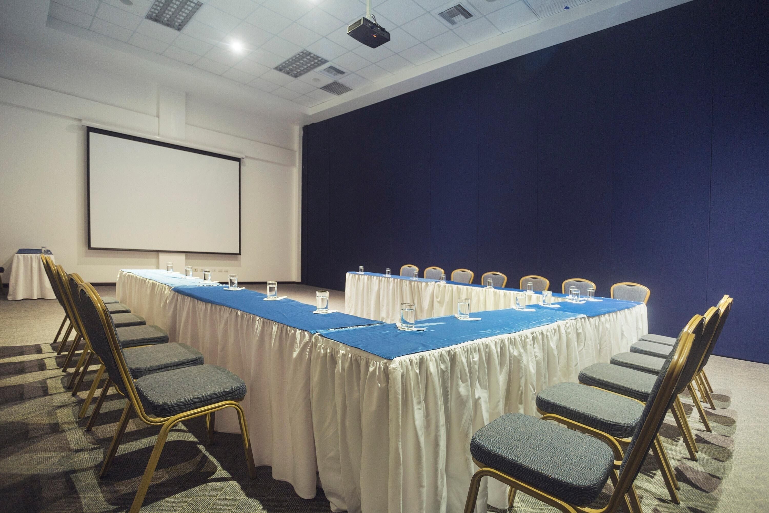 A conference room with a long table, chairs, a projector screen, and a whiteboard.