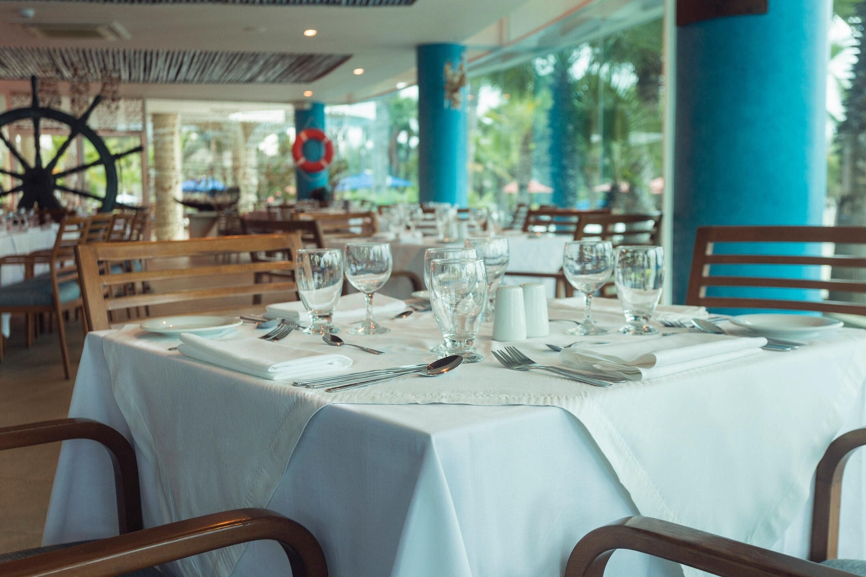 Une table de restaurant dressée avec une nappe blanche, des verres, des couverts et des salières et poivrières.