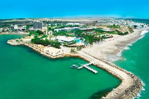 Vista aérea de un complejo turístico costero con puerto deportivo, playa y diversos edificios.
