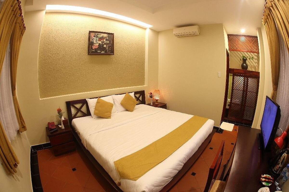 A hotel room with a large bed, a TV, a desk, and a wall-mounted air conditioner.