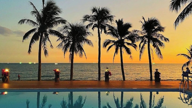 A poolside view with palm trees and a sunset over the ocean. - Thai Hoa Resort (Mui Ne)