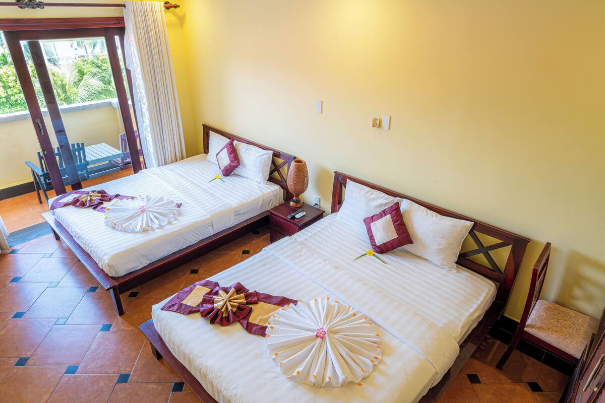 Two beds with white linens and decorative towels, a wooden headboard, and a small bedside table with a lamp.