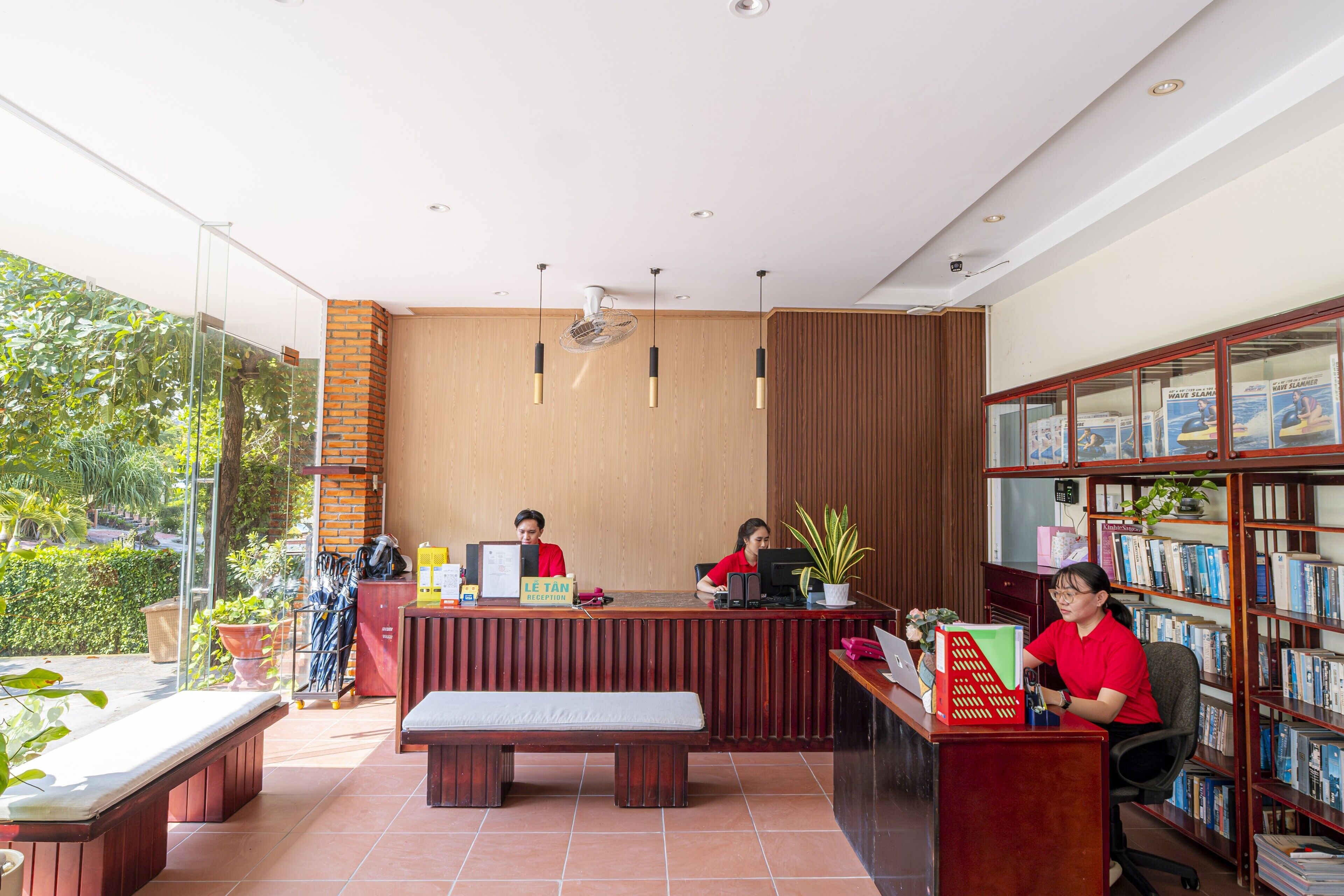Un área de recepción con mostrador, dos empleados, un ventanal grande y una estantería llena de libros.