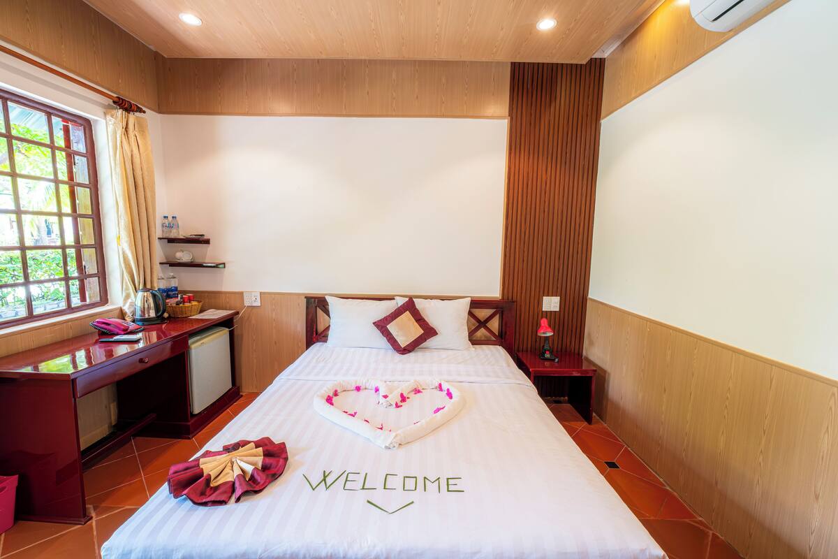 A hotel room with a bed, a desk, a nightstand, and a window.