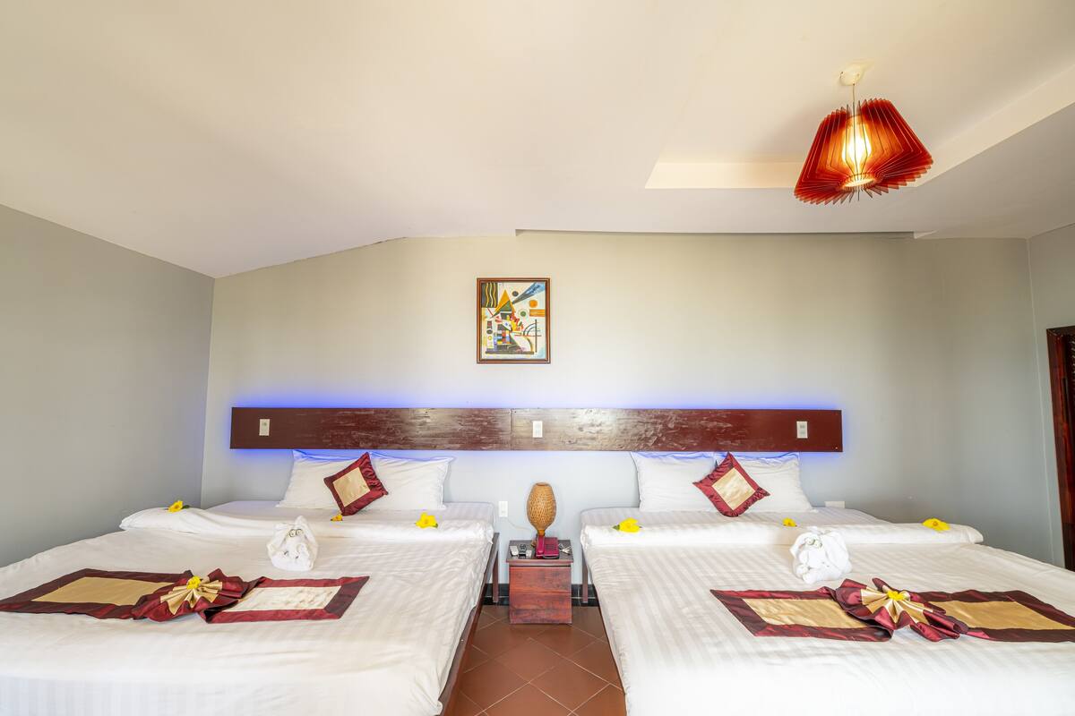 A hotel room with two beds, a wooden headboard, a painting on the wall, and a red hanging light fixture.