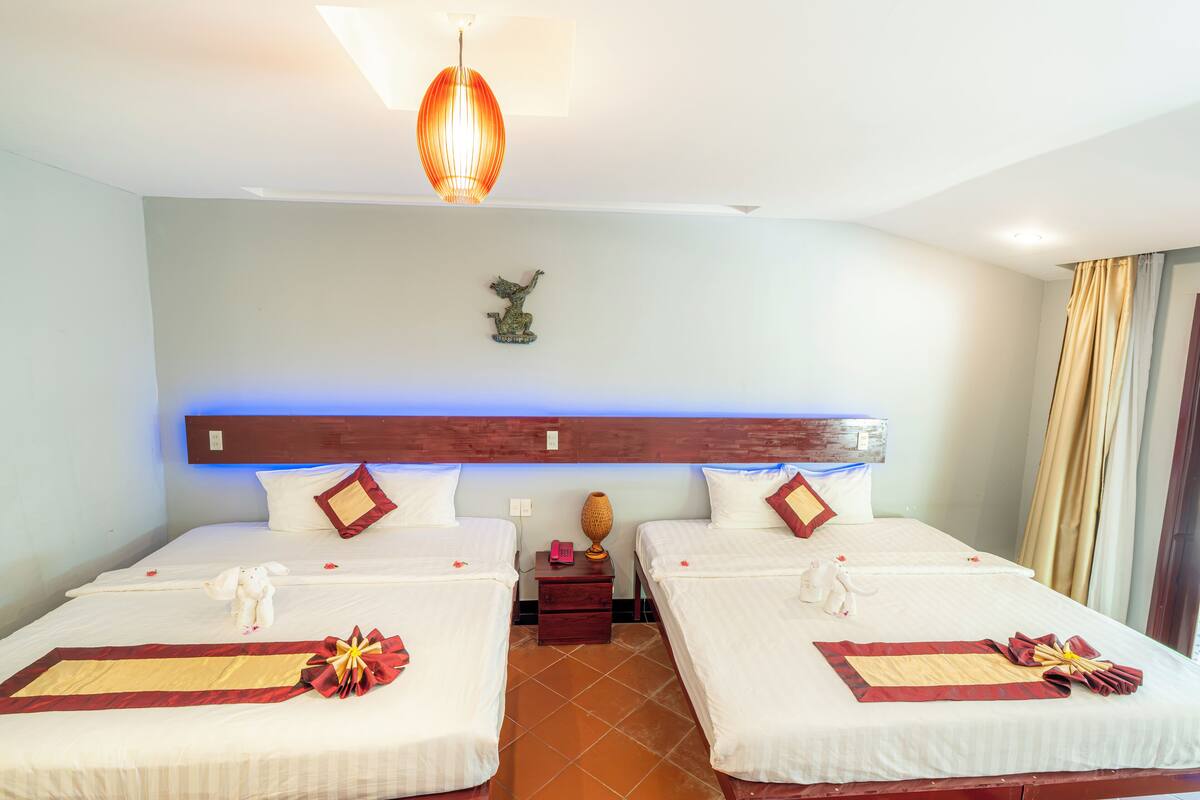 A hotel room with two beds, a wooden headboard, a decorative wall piece, and a nightstand with a lamp.