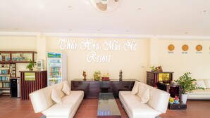 A lobby with two white sofas, a glass coffee table, a reception desk, a refrigerator, and a wall with city names. - Thai Hoa Resort (Mui Ne)