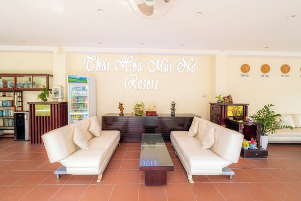 A lobby with two white sofas, a glass coffee table, a reception desk, a refrigerator, and a wall with city names. - Thai Hoa Resort (Phan Thiet)