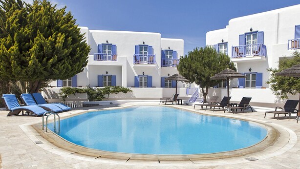 A swimming pool surrounded by lounge chairs and a building with white walls and blue shutters. - Anatolia Hotel (Mykonos)