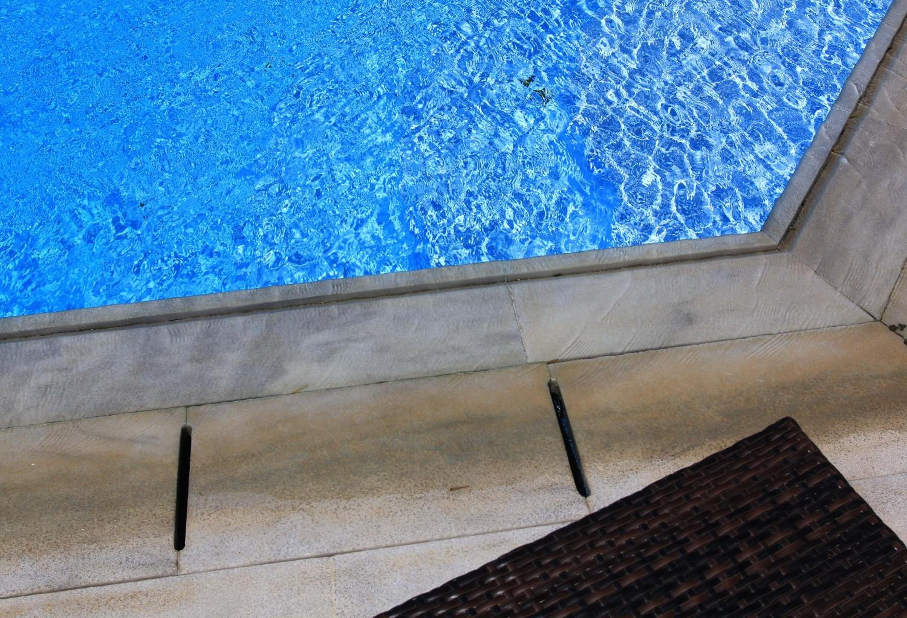 A pool with clear blue water, a stone ledge, and a dark textured mat.