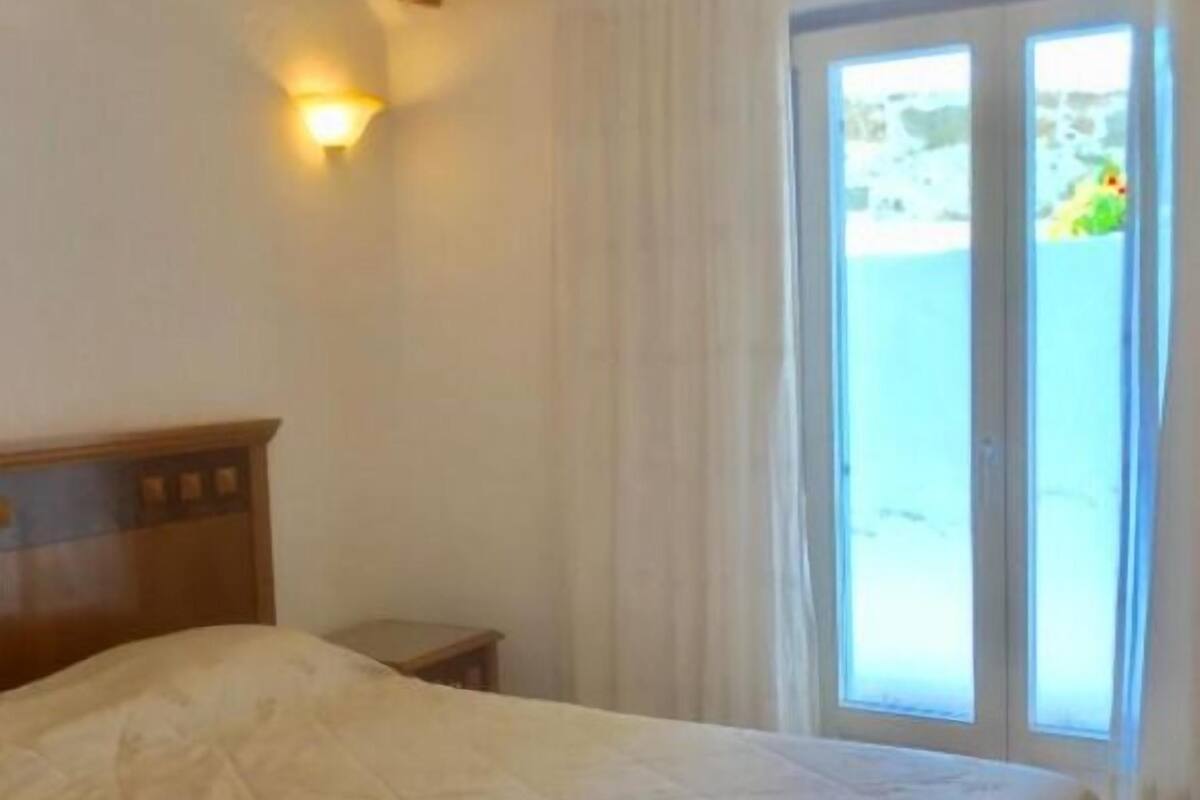 A bedroom with a bed, a nightstand, a wall-mounted lamp, and a sliding glass door leading to a balcony.