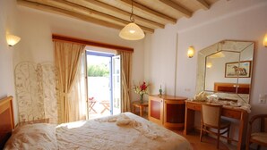 A bedroom with a bed, a desk, a chair, a mirror, and a window with curtains. - Anatolia Hotel (Mykonos)