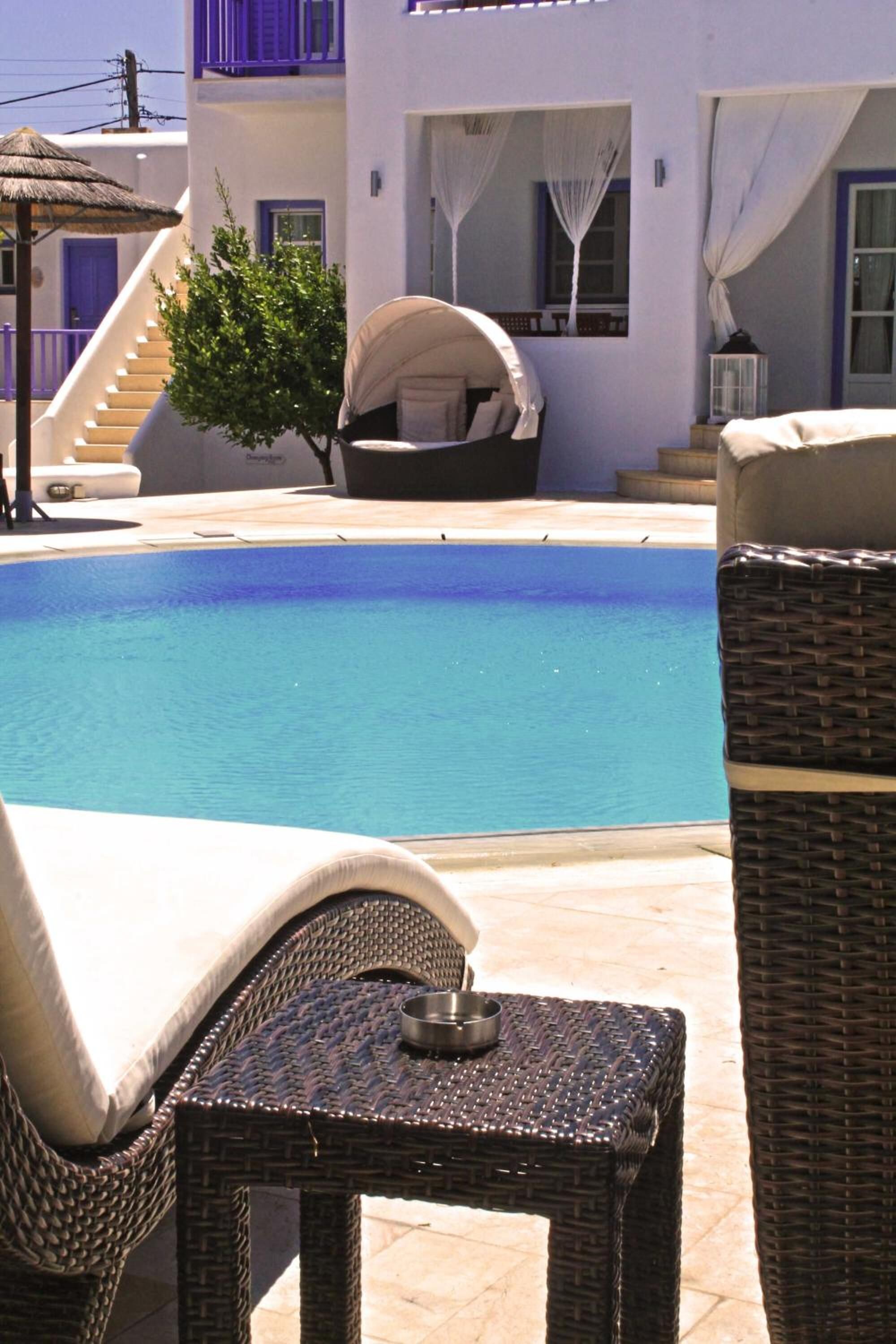 A pool area with wicker furniture, a small table with a bowl, and a building with purple accents and a staircase.
