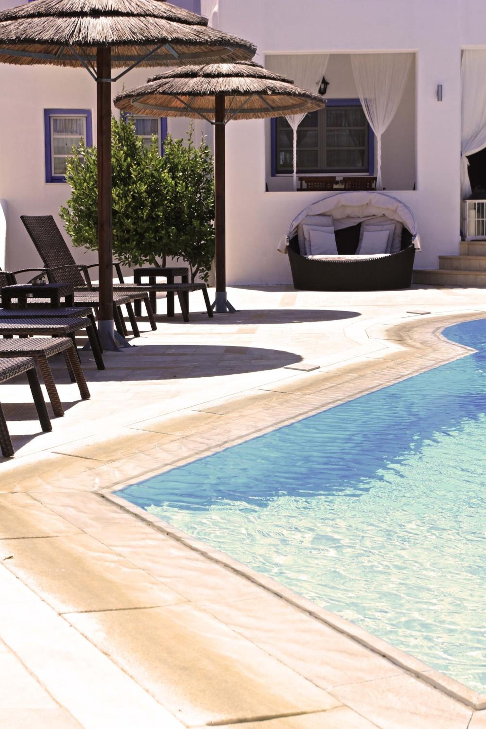 Zona de piscina con sillones de descanso y sombrillas, un jacuzzi y una piscina azul cristalina.