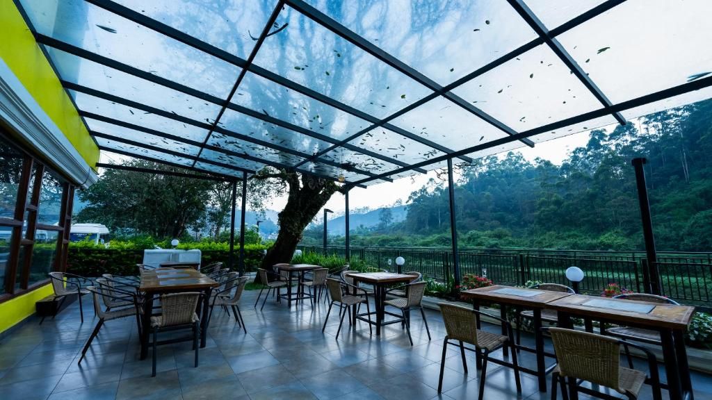 An outdoor patio with tables and chairs, surrounded by glass panels and a view of a forested area.
