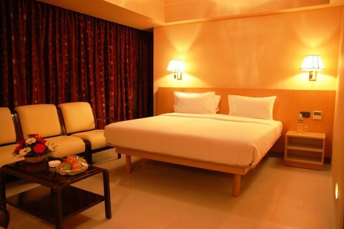 A hotel room with a bed, two bedside lamps, a nightstand, a sofa, and a coffee table with flowers.