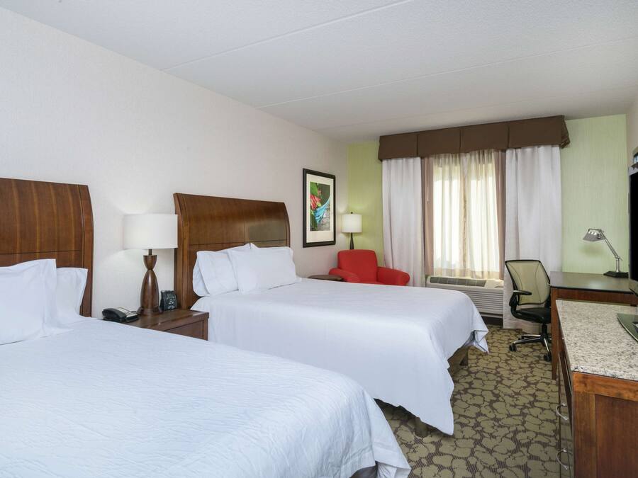 A hotel room with two beds, a desk, a chair, a TV, and a window with curtains.