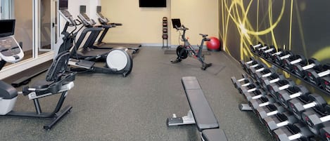A gym with treadmills, stationary bikes, a rowing machine, and a wall-mounted TV.