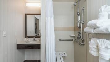 A modern bathroom with a shower, a sink, and a mirror. There are towels hanging on the wall.