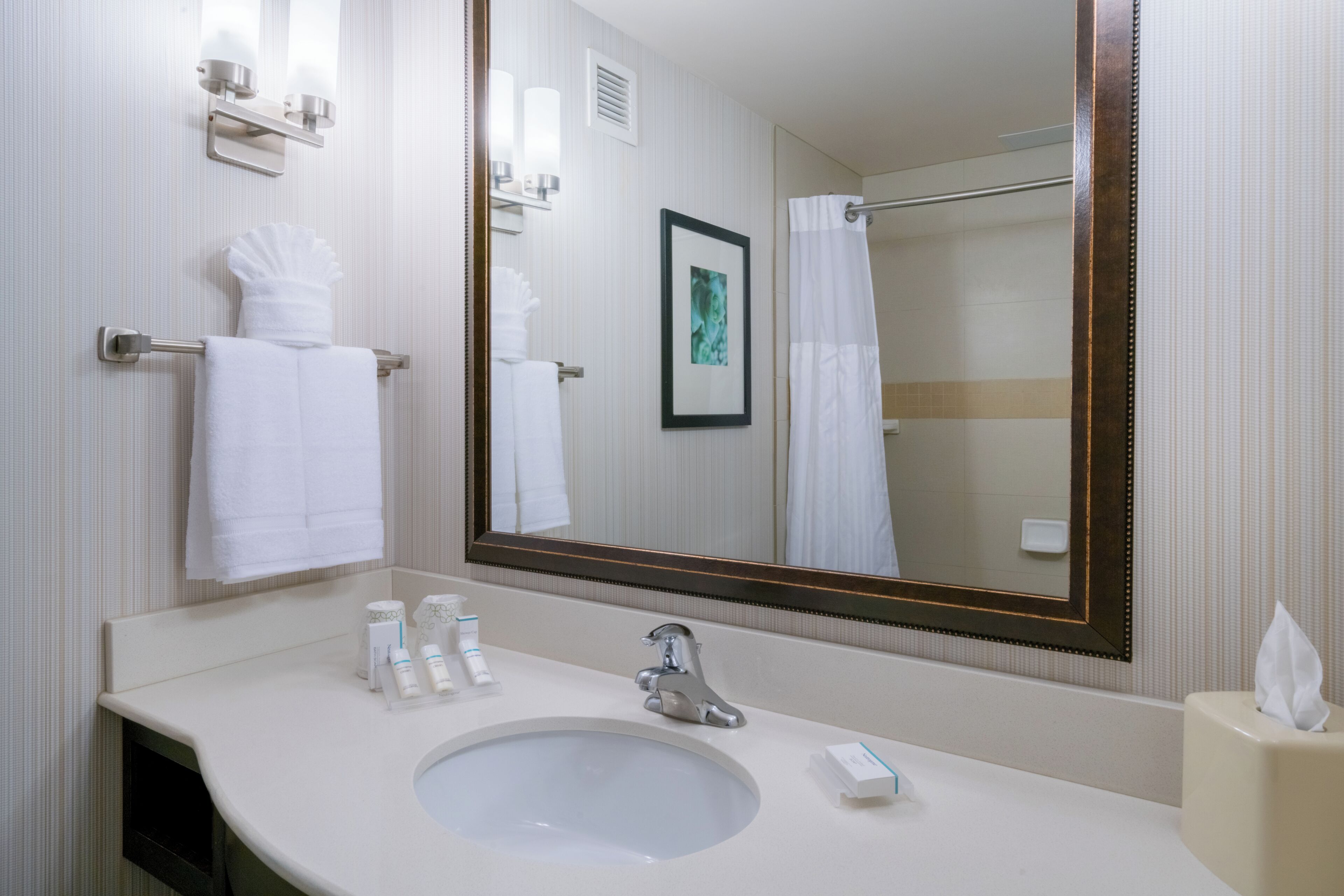 Un baño de hotel con lavamanos, espejo, toallero y artículos de aseo.