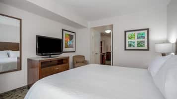 Ein Hotelzimmer mit einem großen Bett, einem Fernseher auf einem Holzbalken, einem Sessel und zwei gerahmten Bildern an den Wänden.