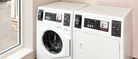 A front view of a modern laundry room with two white washing machines and dryers, a window, and a tiled floor.