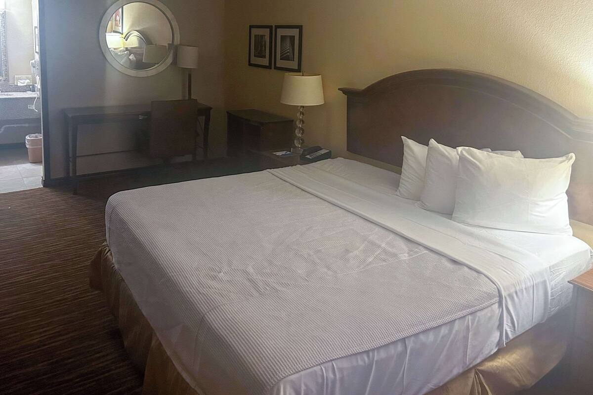 Een hotelkamer met een groot bed, een nachtkastje, een lamp, een spiegel en een klein bureau met een stoel.