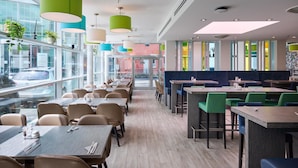 Un restaurante moderno con una combinación de asientos tipo cabina y mesas, ventanas amplias e iluminación colgante colorida.