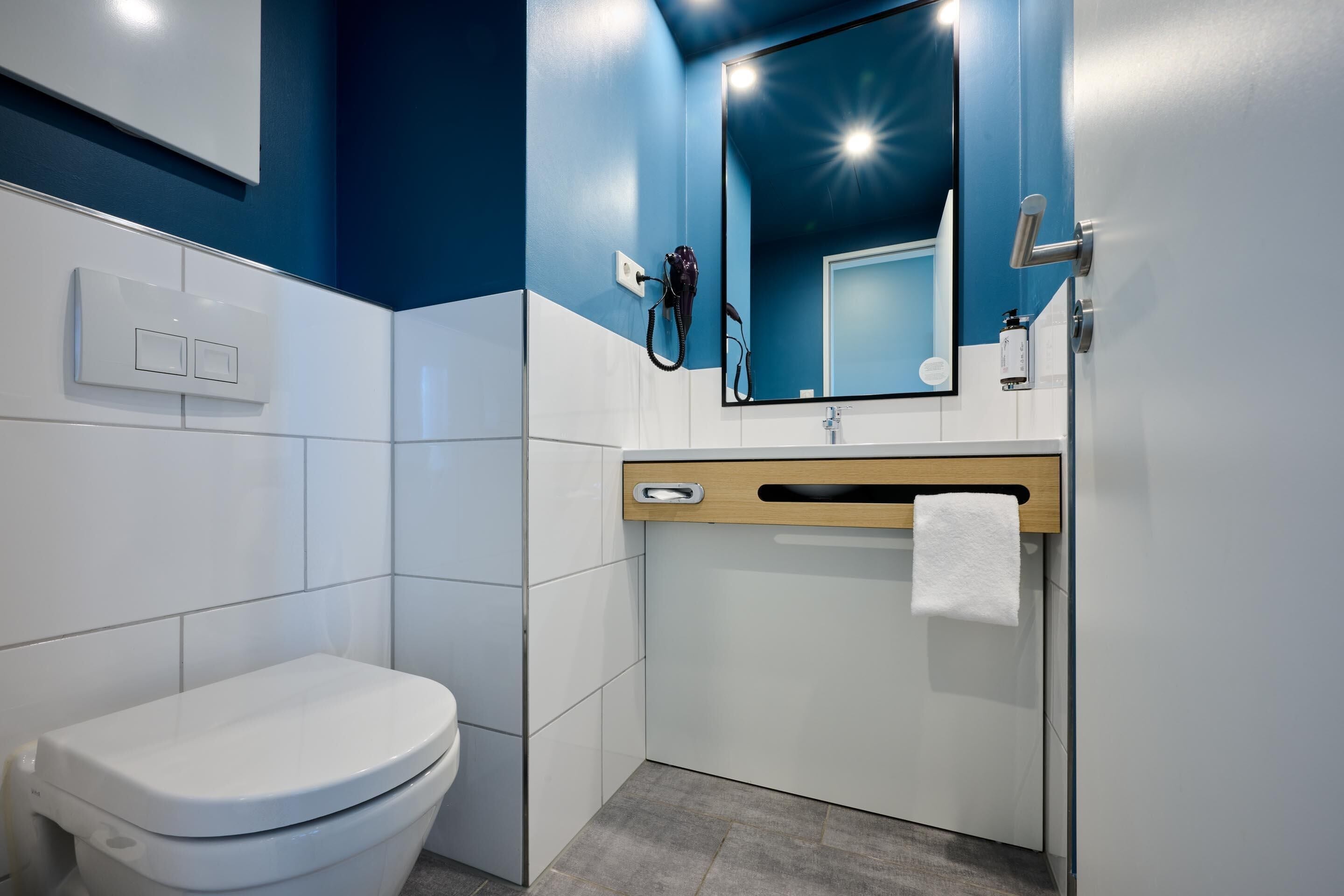 A modern bathroom with a white toilet, a wooden vanity, a mirror, and a towel rack.