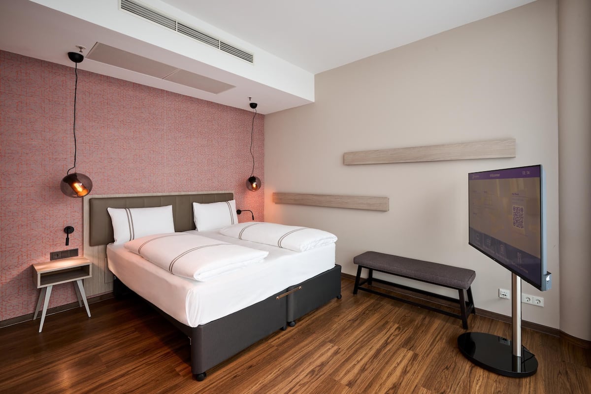 A modern bedroom with a bed, bedside tables, a bench, a TV, and a wall-mounted shelf.
