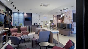 Un moderno vestíbulo de hotel con áreas de descanso, un mostrador de recepción y una pantalla de televisión.